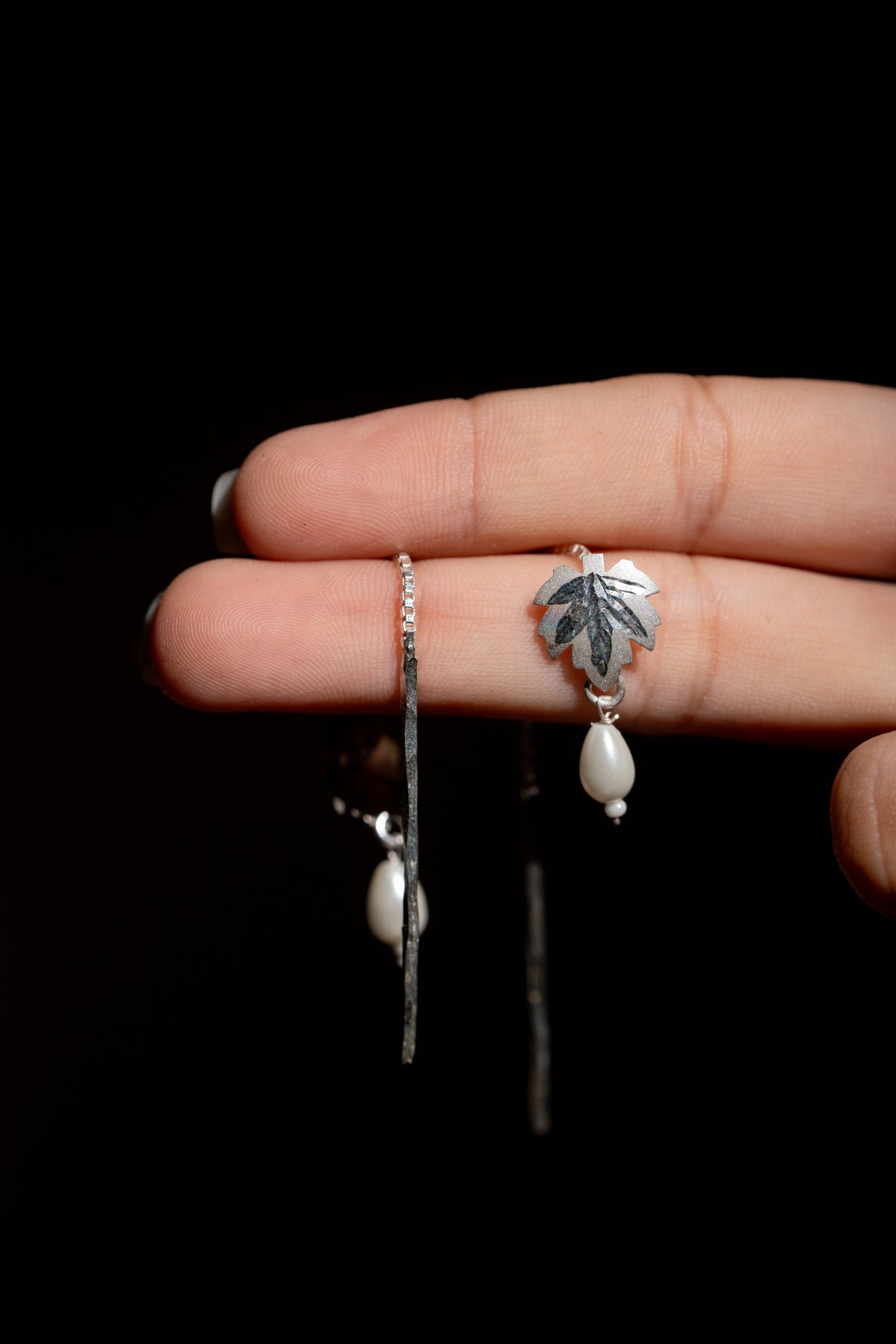Hand holding a silver Earring with a leaf design and pearl drop 