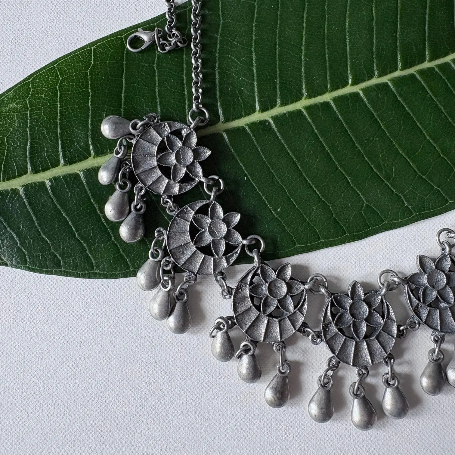 Chandrapushpa oxidised brass tribal ring with engraved motif and draped chain styling, displayed with a white fabric wrap on green leaf – Complimento artisan accessory.