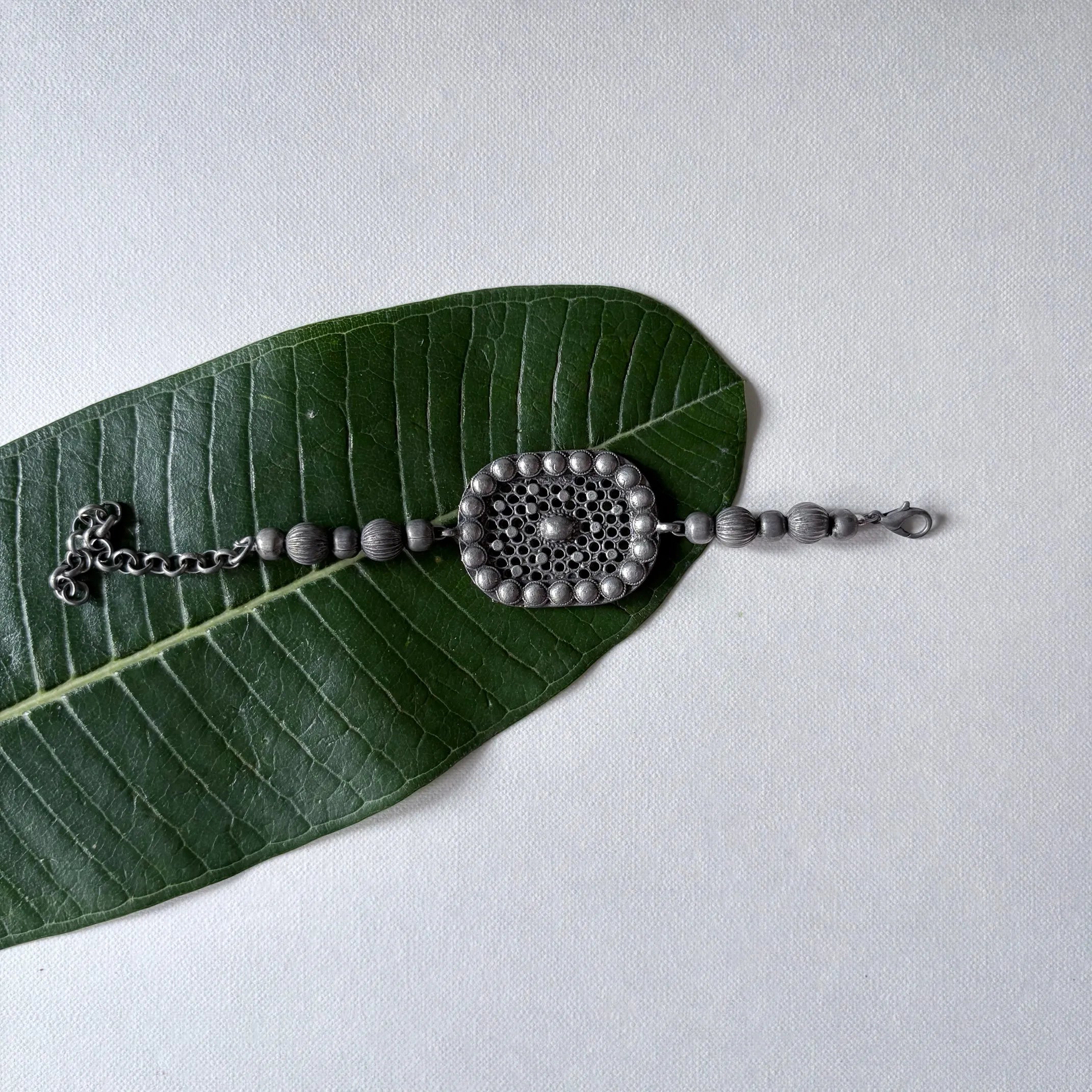 Flatlay of Jalakriti oxidised brass ball bracelet with central tribal motif and bead detailing – Complimento